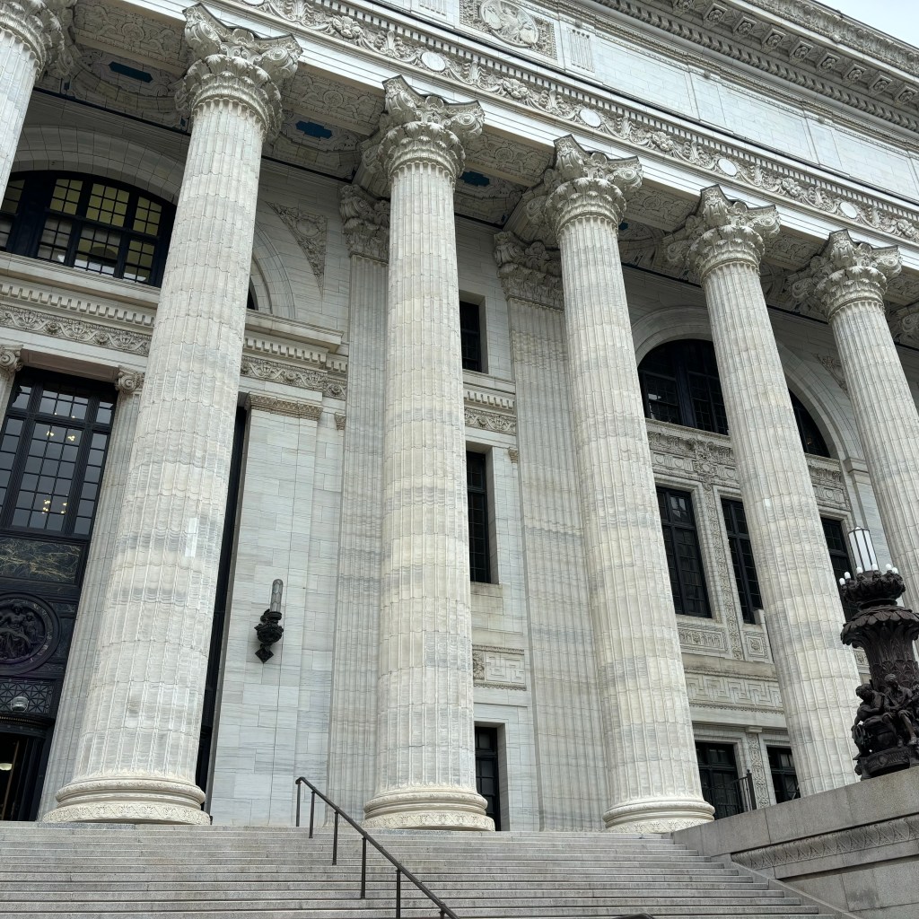 Exterior of a grand building with tall Corinthian columns, intricate architectural detailing, and a wide staircase leading to the entrance.
